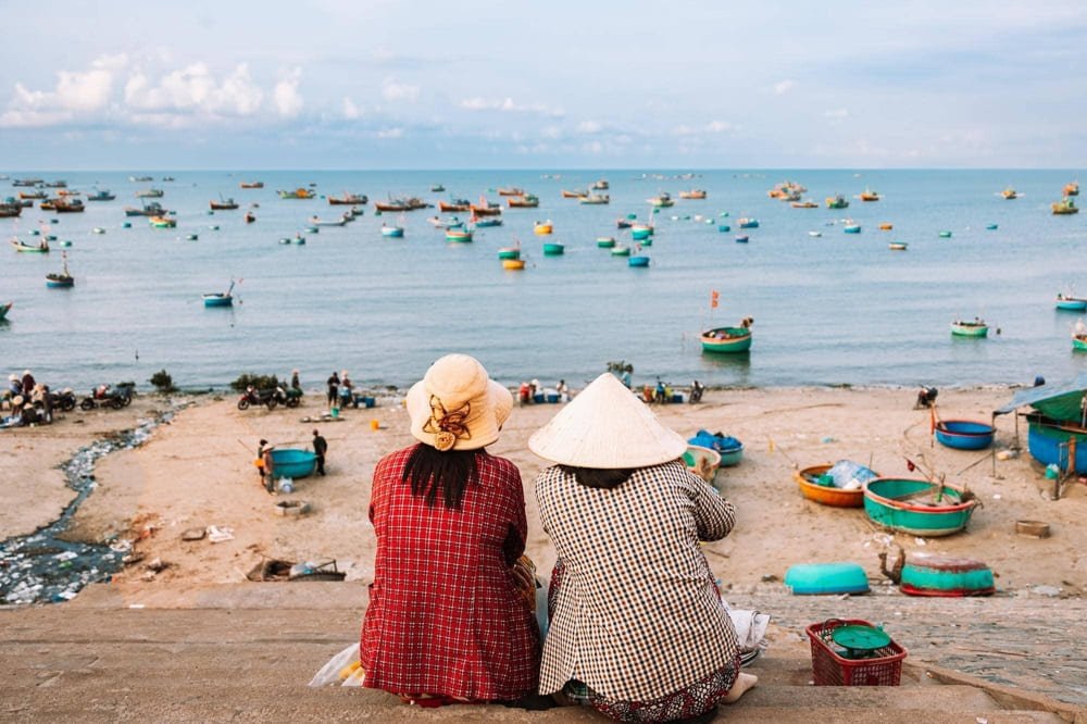 Mui Ne Beach at sunset with colorful fishing boats and kitesurfers enjoying the perfect wind conditions
